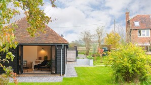 Un acogedor cottage con techo inclinado, un pequeño porche y un jardín bien cuidado.