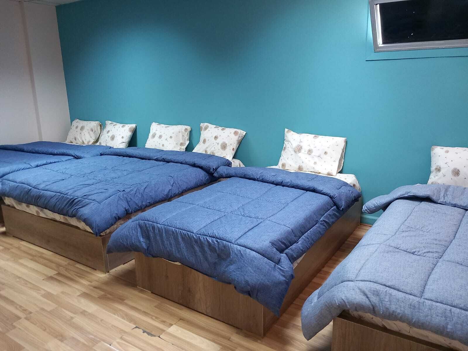 A room with two beds, each with a blue bedspread, and a teal wall.