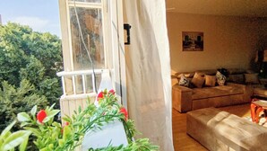 A cozy living room with a sofa and a coffee table, a window with a view of trees, and a potted plant with red flowers. - Garden City Apartment in Downtown Cairo (Cairo)