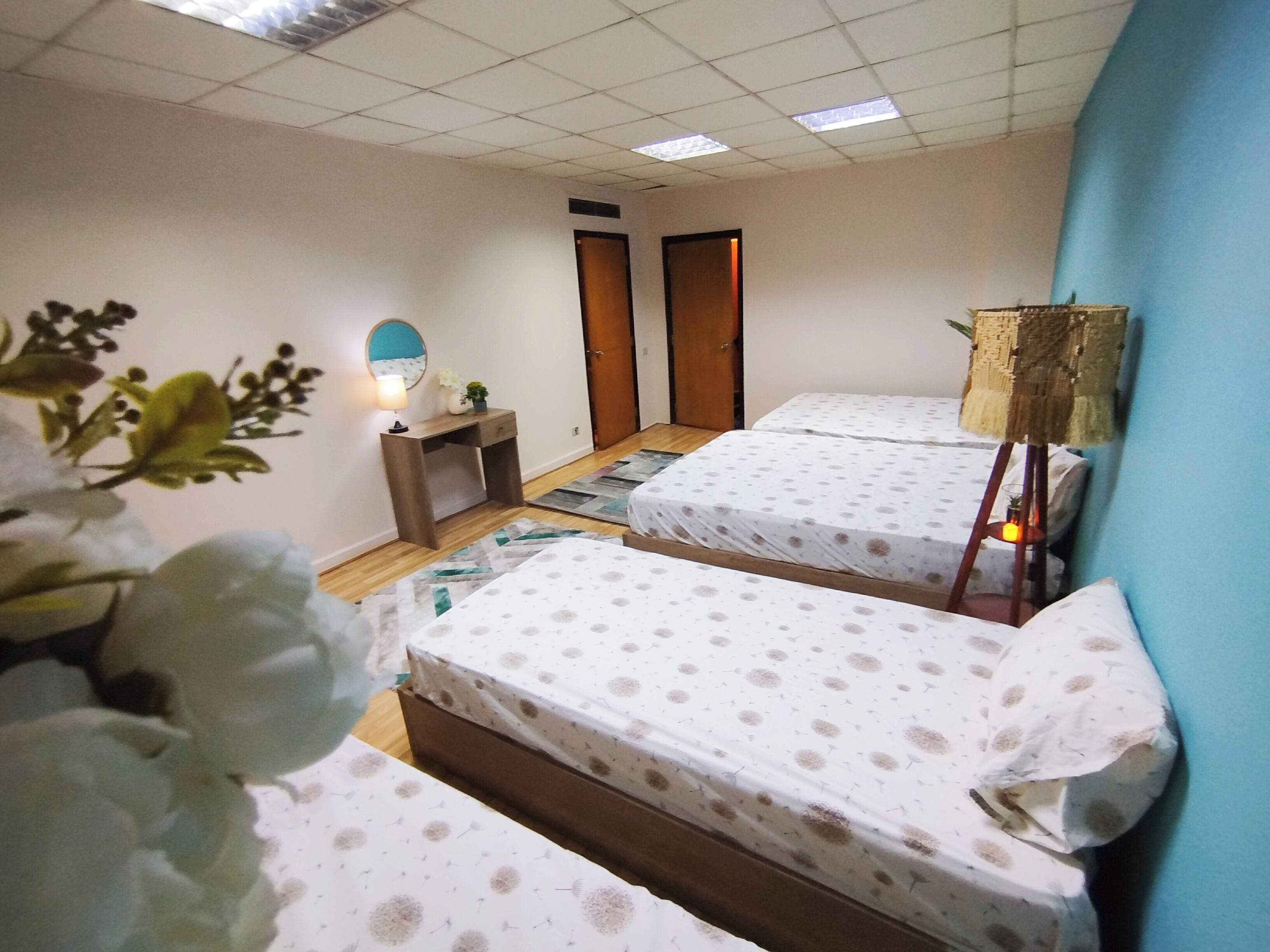 A hotel room with two beds, a desk, a lamp, and a door.
