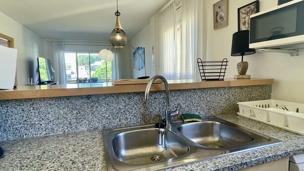 A kitchen with granite countertops, stainless steel sink, and a hanging pendant light.