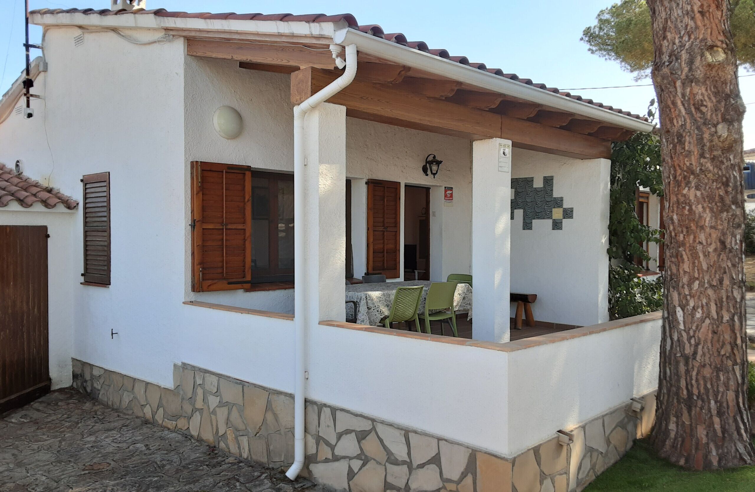 A white building with a stone foundation, wooden shutters, and a tiled roof.