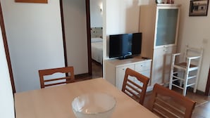 Un coin repas avec une table, des chaises, un téléviseur posé sur un meuble et un lit en arrière-plan.