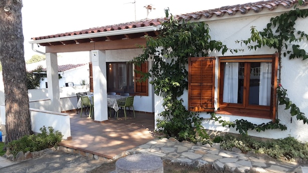 Une maison avec un toit en tuiles, des volets en bois et un patio couvert comprenant une table et des chaises.