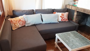 Un salon moderne avec un canapé d’angle, des coussins à motifs et une petite table.