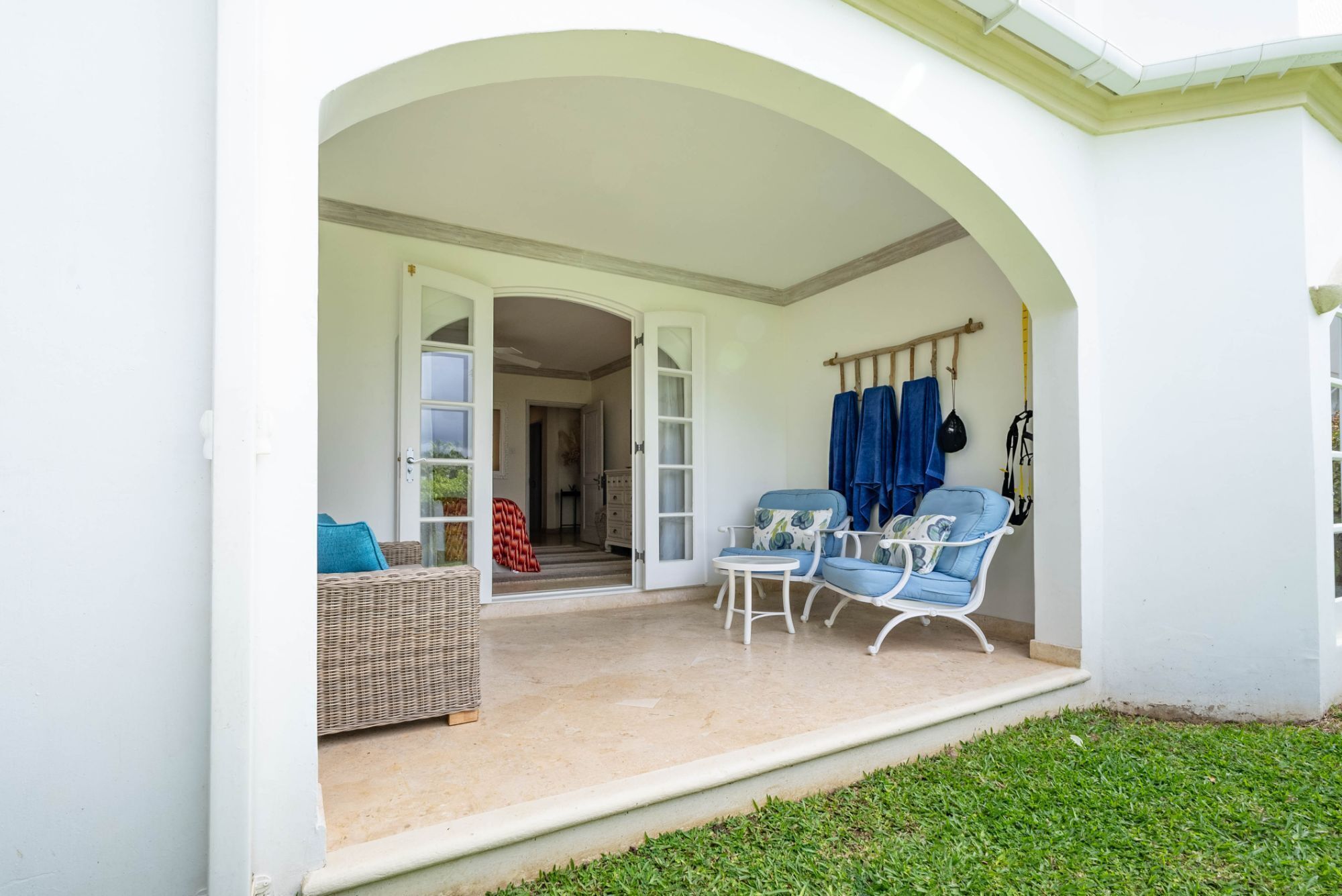 An open patio with wicker furniture and a white chair, a small table, and a blue towel rack.