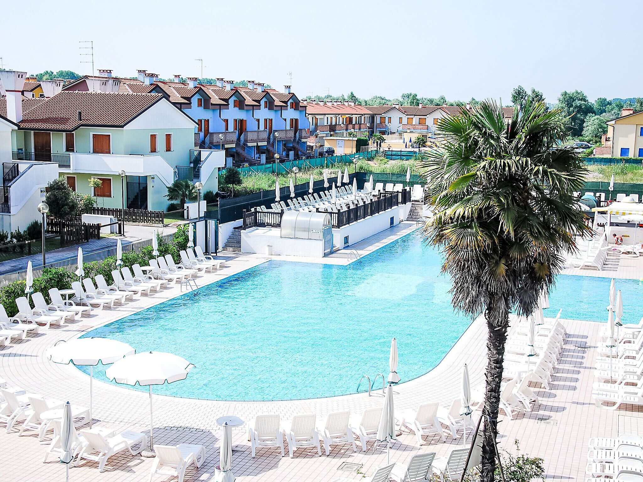A swimming pool with lounge chairs and umbrellas, surrounded by buildings with red-tiled roofs.