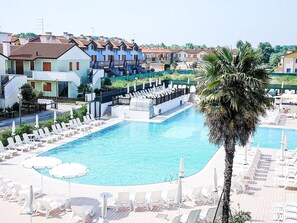 A swimming pool with lounge chairs and umbrellas, surrounded by buildings with red-tiled roofs. - Mediterraneo by Interhome (Rosolina Mare)