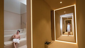Un espace de détente avec une personne assise sur un banc, un couloir avec un miroir et une plante.