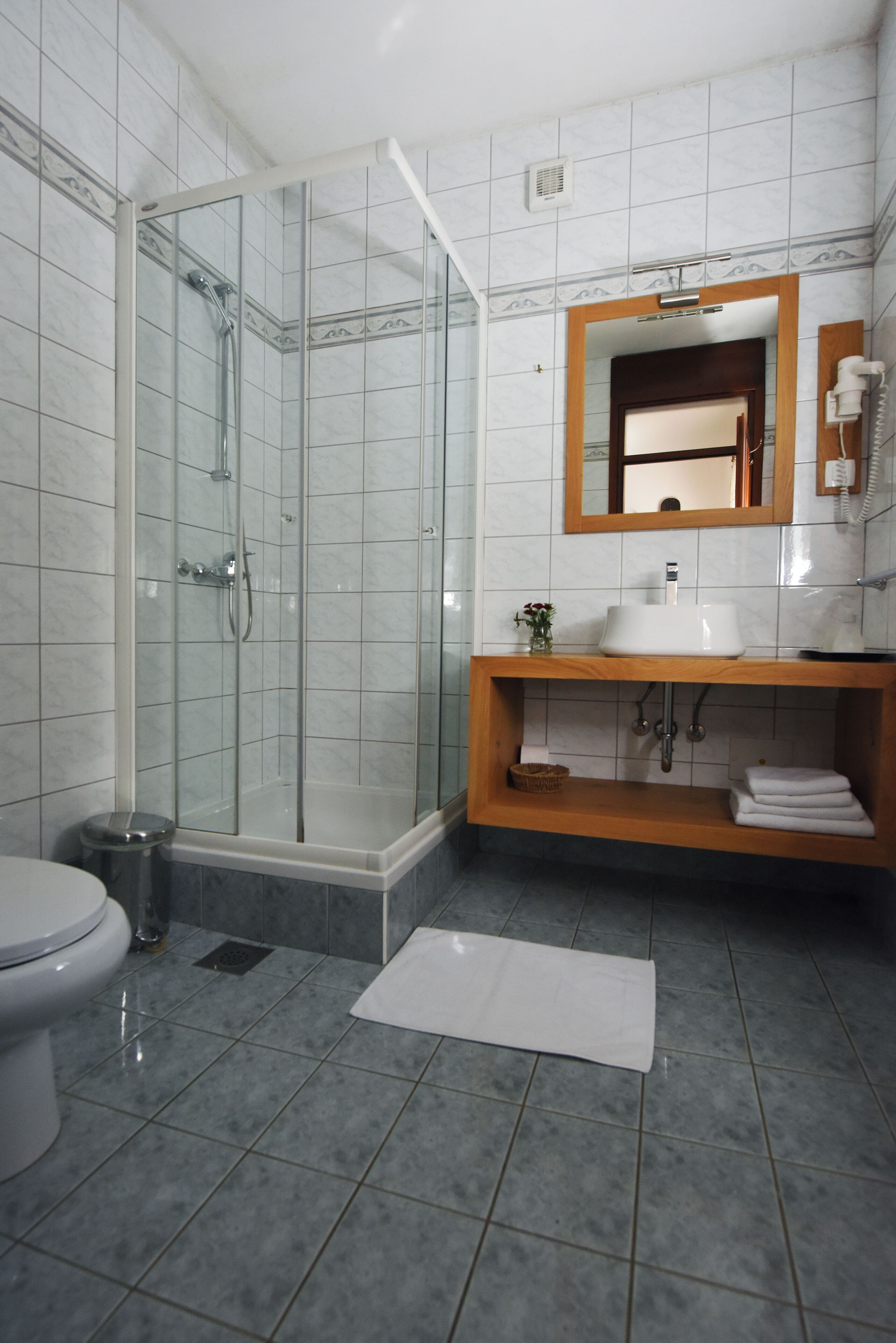 Een badkamer met een douchecabine van glas, een witte wastafel en een houten wastafelmeubel.