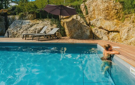 A swimming pool with a wooden deck, lounge chairs, and a large umbrella.