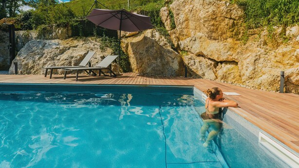Une piscine avec une terrasse en bois, des chaises longues et un grand parasol.