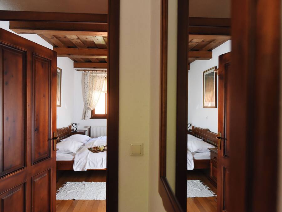 Ein Schlafzimmer mit Holzboden, einem Bett mit weißen Leinen, einem Nachttisch und einem Fenster mit Vorhängen.