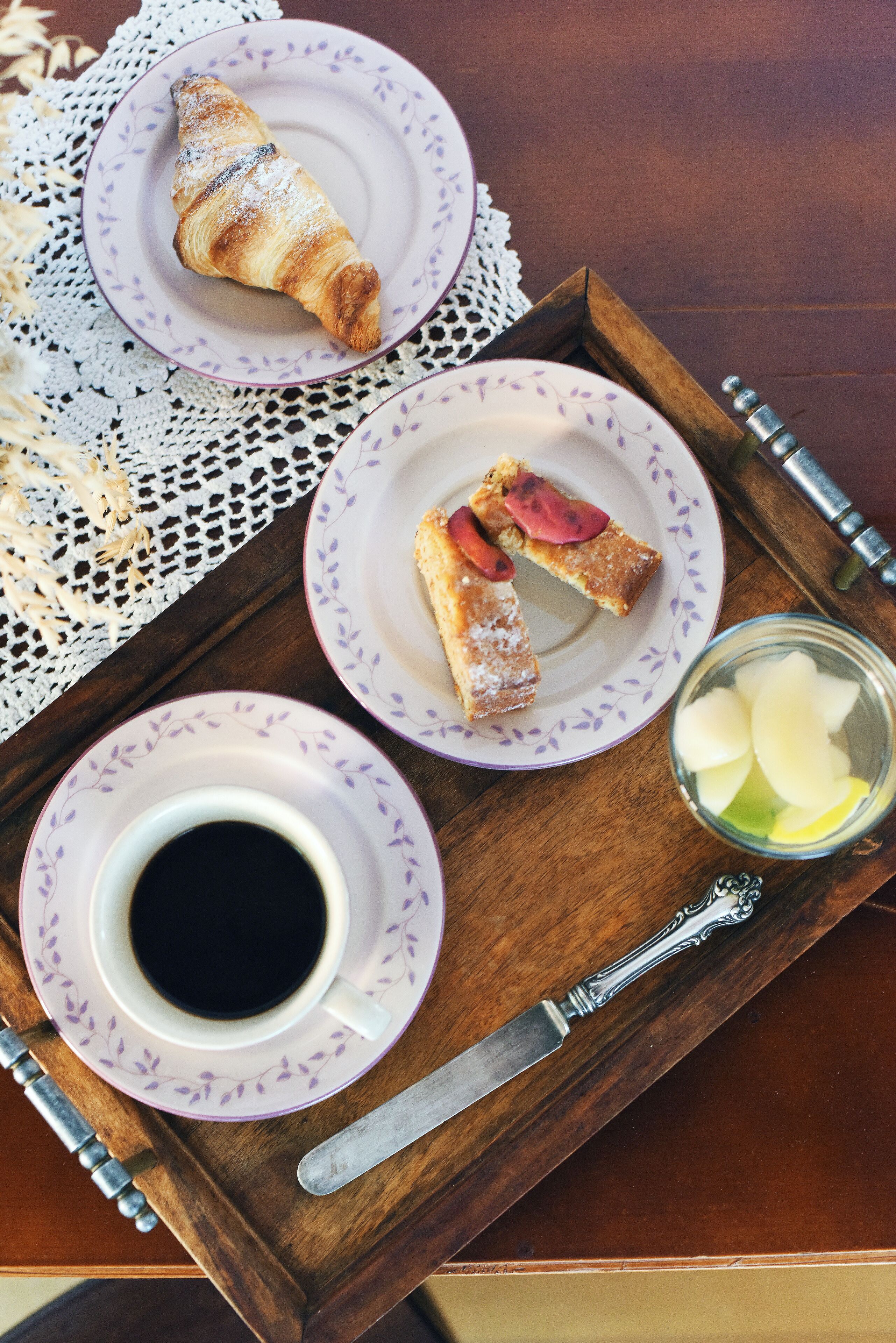 Un plateau avec un croissant, une part de gâteau aux fraises, une tasse de café et un verre d’eau.