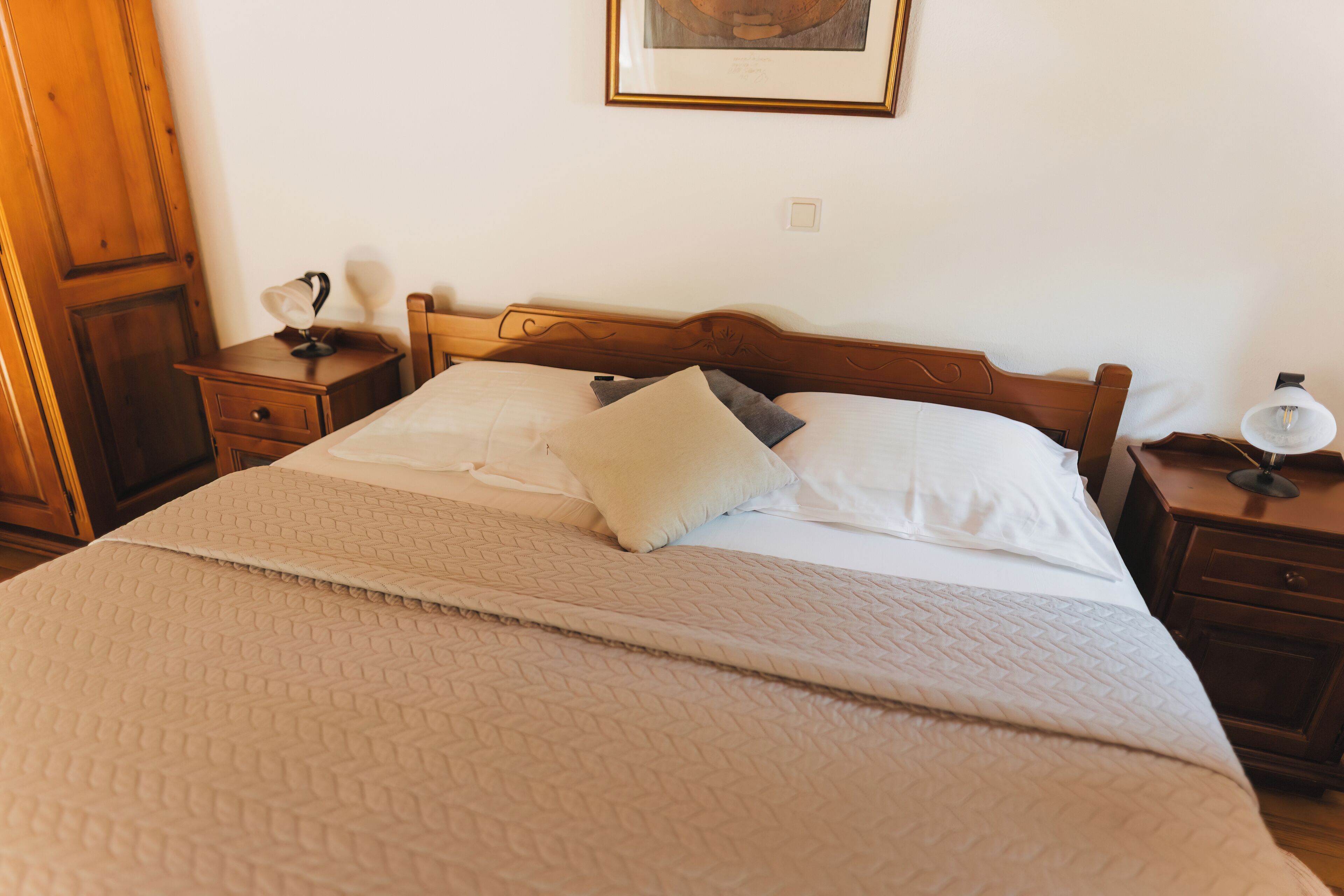 Un letto ben rifatto con copripiumino trapuntato e cuscini, una testiera in legno, un comodino con una lampada e un quadro appeso al muro.