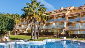 Una piscina con agua cristalina azul, rodeada de césped cuidado y palmeras.