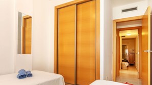 Habitación de hotel con dos camas, un armario de madera, un espejo y un baño visible a través de una puerta abierta.