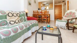 Un salón acogedor con un sofá, una mesa baja con pasteles, y un comedor con muebles de madera.