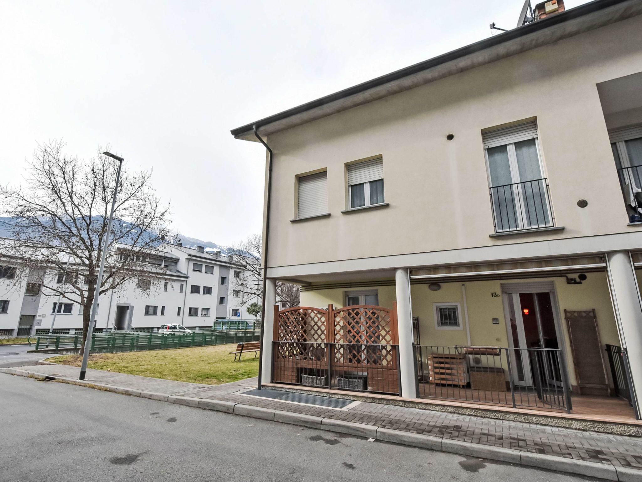 Un immeuble résidentiel doté d’une entrée abritée, d’un petit espace extérieur aménagé pour s’asseoir et offrant une vue sur une montagne en arrière-plan.