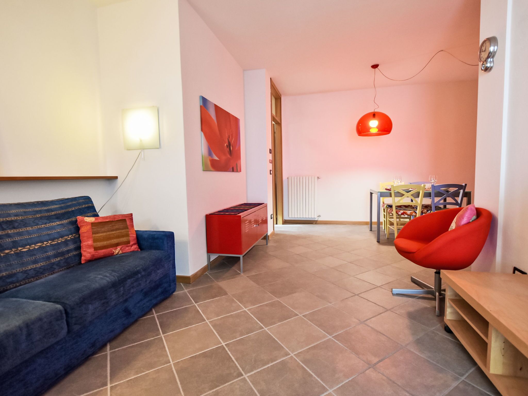A modern living room with a blue sofa, red cabinet, and a red chair.