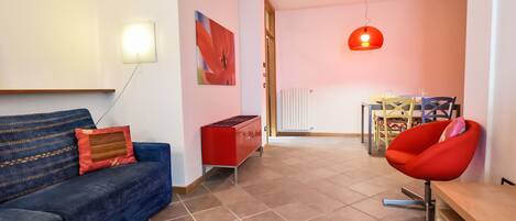 A modern living room with a blue sofa, red cabinet, and a red chair.