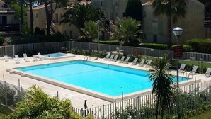 A rectangular swimming pool surrounded by a white fence, with lounge chairs and palm trees. - Coastal Comfort in Agde (Agde)