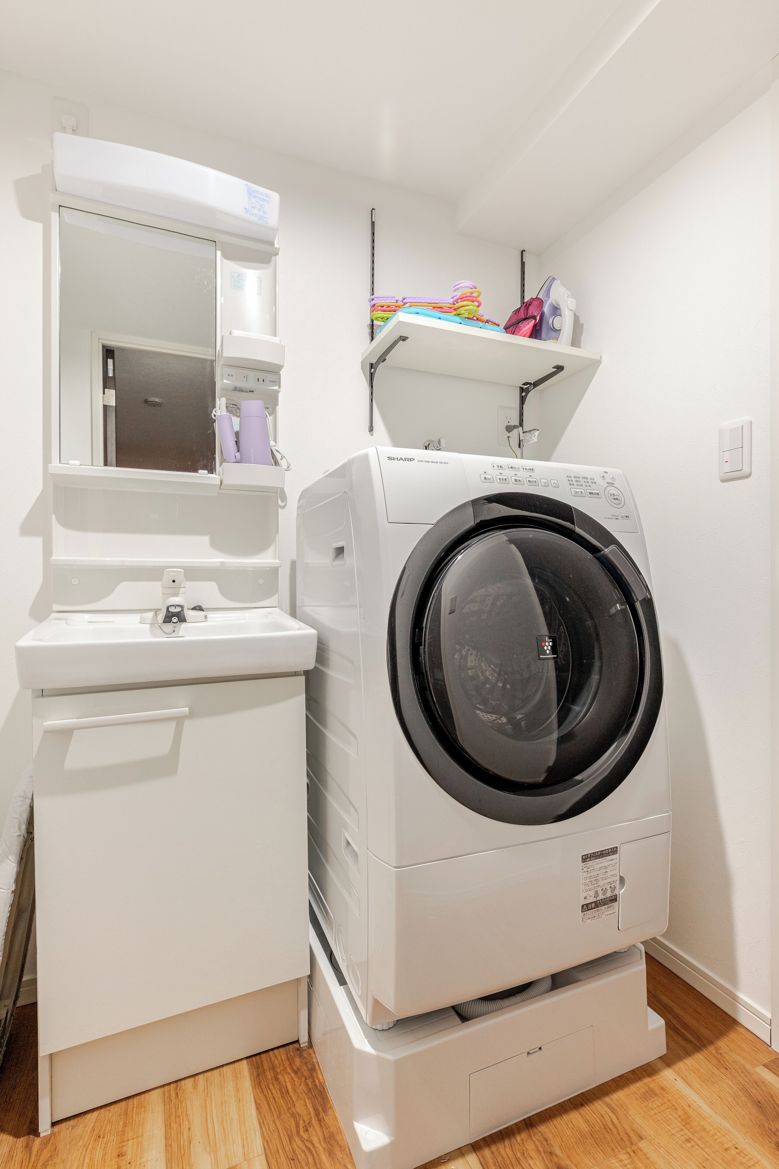 Une petite buanderie équipée d’un lave-linge et d’un sèche-linge à chargement frontal, d’un petit évier et d’un miroir au-dessus de l’évier.