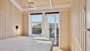 Une chambre avec un grand lit, des murs en bois, une porte-fenêtre coulissante donnant sur un balcon et un luminaire au plafond.