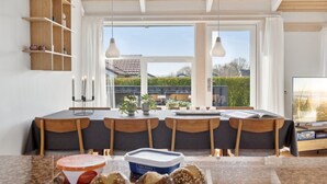 Une cuisine moderne dotée d’un grand îlot central, de chaises en bois, d’une table à manger et offrant une vue sur l’extérieur.