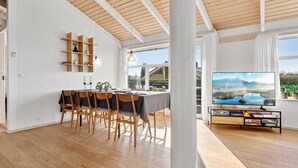 Un salon moderne comprenant un coin repas, un plancher en bois, une grande fenêtre offrant une belle vue et un téléviseur à écran plat posé sur un meuble.