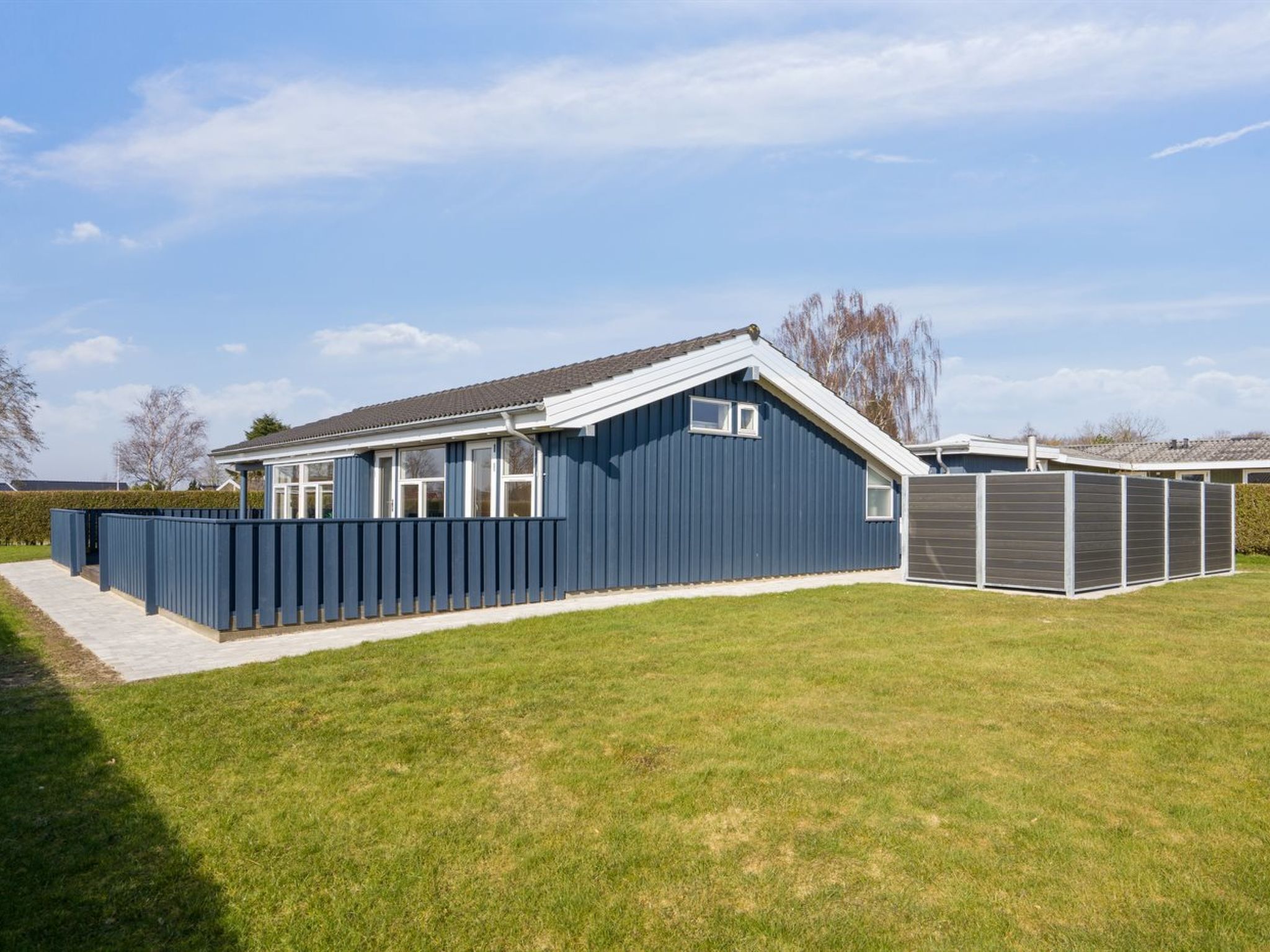 A modern single-story house with a sloped roof, large windows, and a fenced backyard.