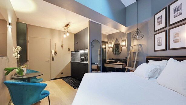 Une chambre d’hôtel moderne dotée d’un grand lit, d’un petit coin repas avec une table et des chaises, d’une kitchenette et d’une salle de bain.