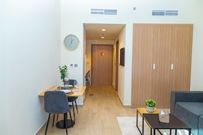 A modern living room with a sofa, a dining area with a table and chairs, and a hallway leading to a wooden door.