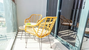 A balcony with wicker chairs and a small table, large windows, and a glass door. - Bloomfields STU View Azizi Riviera (Dubai)