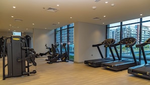 A modern gym with treadmills, weight machines, and a large window offering a view of the city. - Bloomfields STU View Azizi Riviera (Dubai)