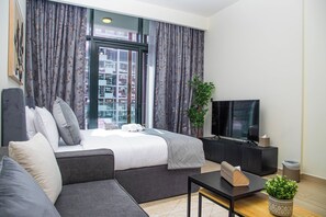 Habitació d'hotel moderna amb llit, sofà, televisió i una planta en test.