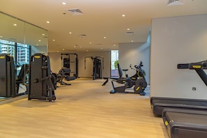A gym with various exercise equipment, a mirror, and a view of the outside.