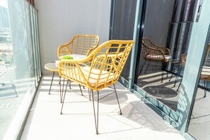 A balcony with wicker chairs and a small table, large windows, and a glass door.