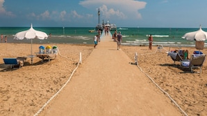 Een strand met een zandpad dat naar de zee leidt, met strandparasols en ligbedden.