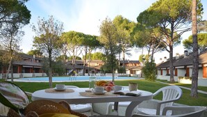 Une table placée au bord de la piscine, avec un livre, des fruits et une bouteille d’eau, le tout entouré d’arbres et donnant sur la piscine.