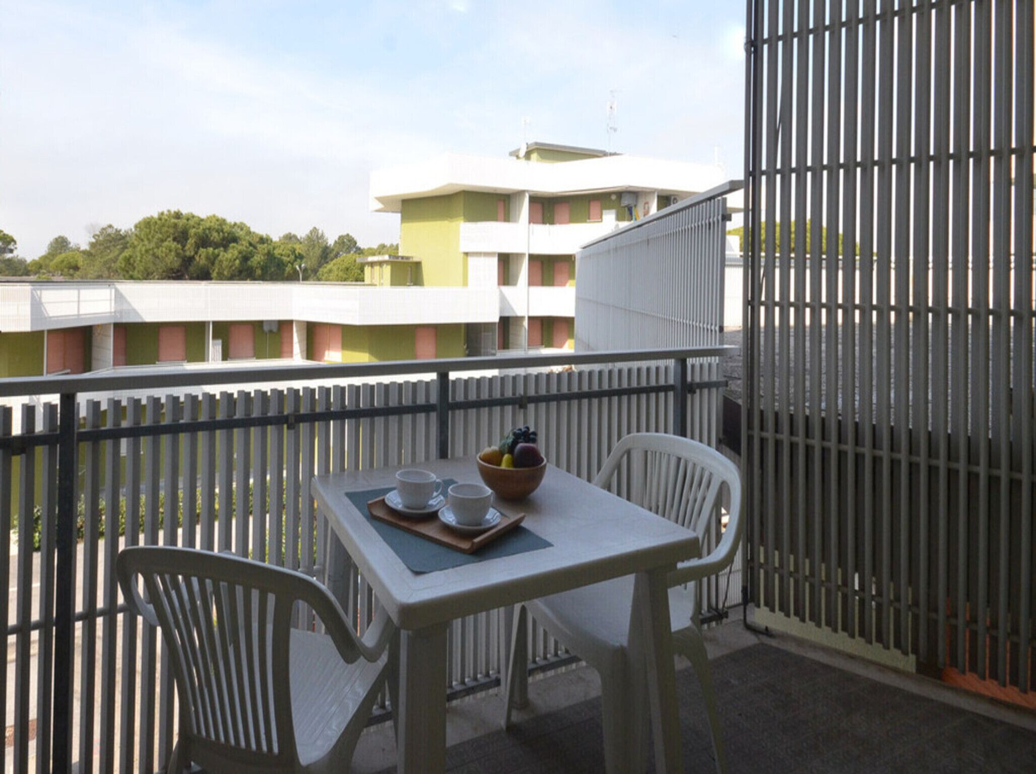 Een balkon met een tafel gedekt voor twee personen, een schaal fruit en twee kopjes.