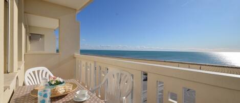 A balcony with a table set for two, overlooking a beach.