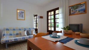 A cozy living room with a sofa, a dining table with a TV, and a window with curtains. - Wonderful villa with shared garden (Bibione)