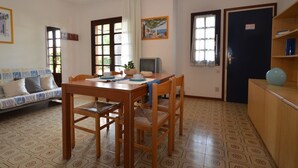 A dining area with a wooden table and chairs, a sofa with patterned cushions, and a television. - Wonderful villa with shared garden (Bibione)