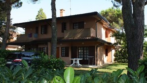 A two-story building with a balcony, surrounded by trees and greenery. - Wonderful villa with shared garden (Bibione)