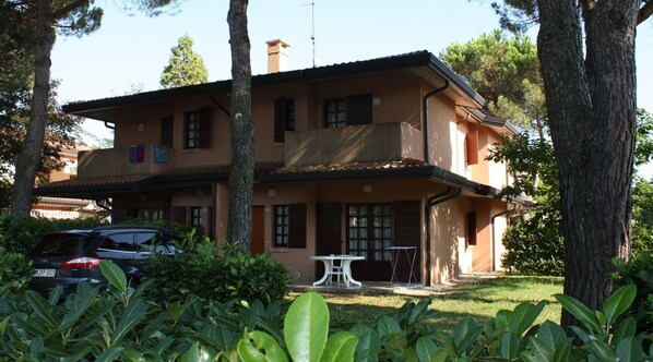 A two-story building with a balcony, surrounded by trees and greenery.