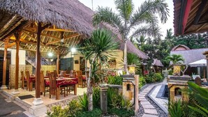 Un restaurante con techos de paja y terraza, rodeado de plantas tropicales y un sendero de piedra.