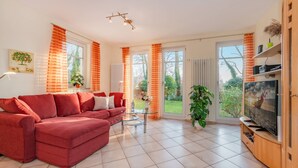 A living room with a red sofa, a glass coffee table, and a TV on a wooden stand. - House Dünenwald 14 - short distances to the beach and the center for 3 persons (Zinnowitz)
