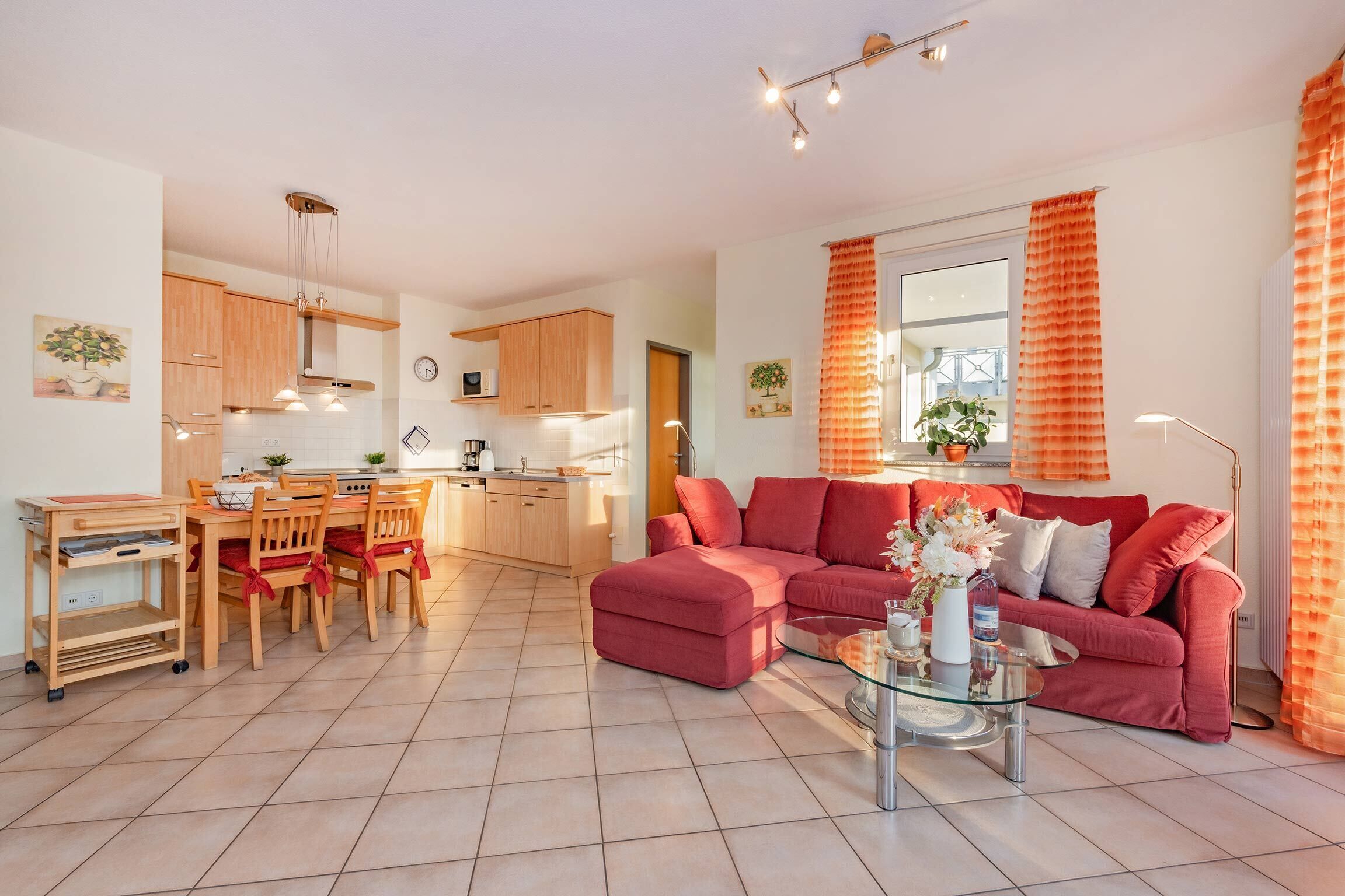 A modern living room with a red sofa, a glass coffee table, and a dining area with wooden furniture.