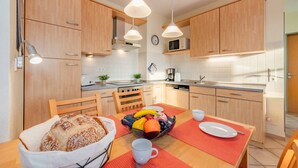 A modern kitchen with wooden cabinets, a dining table with a red placemat, and a fruit bowl. - House Dünenwald 14 - short distances to the beach and the center for 3 persons (Zinnowitz)